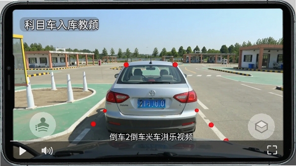 驾考学车APP内播放科目二倒车入库教学视频的画面,视频中教练车正在操作,屏幕上有红色点位标记和文字解说,画质清晰,背景为驾校场地,适合教学演示。