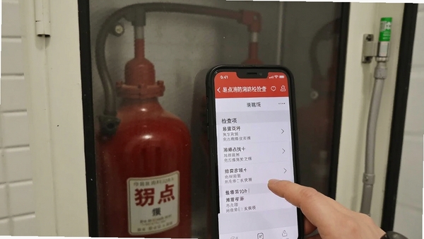 用户正在手机上操作易点消防进行消防栓检查,界面显示检查项列表,背景为室内消火栓箱,实拍风格