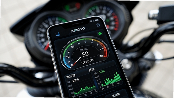 ZXMOTO手机应用界面特写,屏幕上以仪表盘和图表形式清晰显示摩托车电瓶电压、发动机温度等健康数据,界面UI设计科技感强,色彩鲜明,背景为虚化的摩托车仪表台