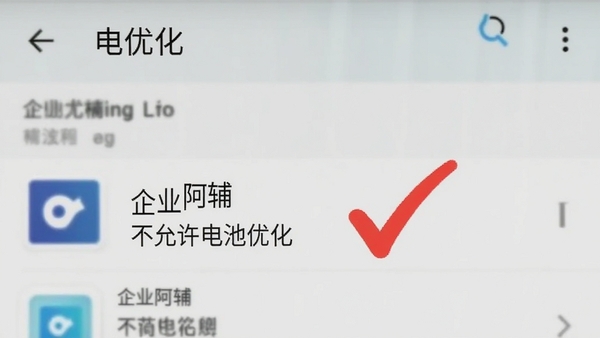 一张手机截图风格的图片,画面显示安卓系统的“电池优化”设置界面,其中“企业阿辅”应用被设置为“不允许电池优化”,旁边用红色对勾标注,背景为设置菜单的模糊效果。