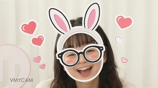VMYCAM趣味贴纸特效演示,画面中人物戴着兔子耳朵和眼镜贴纸,表情开心,周围有漂浮的心形动画。